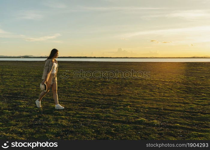 cheerful woman walk across the green field with sunset