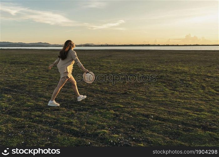 cheerful woman walk across the green field with sunset