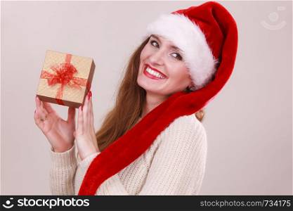 Cheerful woman wearing santa claus hat holding golden gift box with red bow. Christmas time, giving and happiness concept.. Woman holding gift box. Christmas time