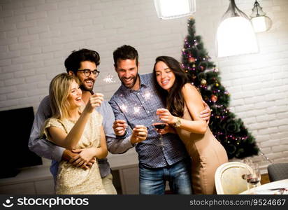 Cheerful women and men celebrating New Year eve with sparkles and wine at home