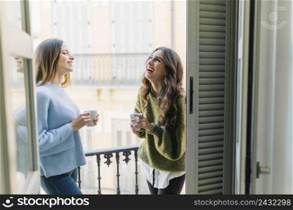 cheerful women with mugs balcony