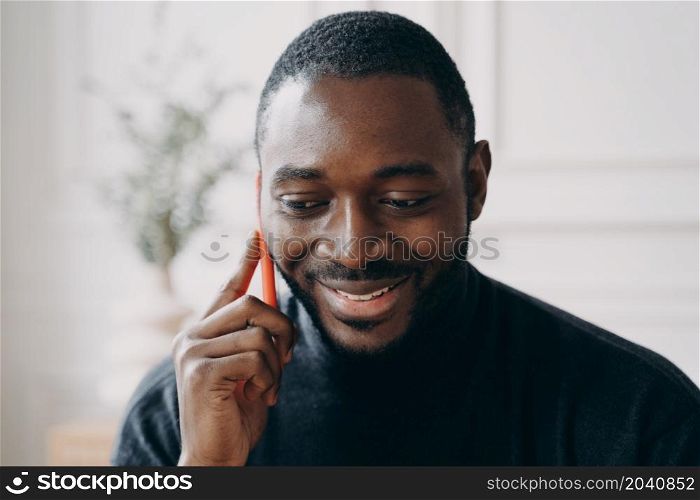 Cheerful young African American businessman talking on smartphone while working distantly in modern home office interior. Mobile communication and freelance, male entrepreneurship concept. Cheerful young African American businessman talking on smartphone while working distantly at home