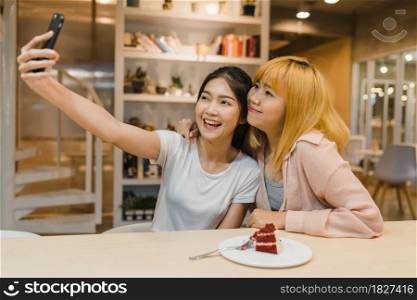Cheerful young Asia friend clicking selfie using mobile phone at a coffee shop. Two joyful attractive Asian girls together at restaurant or cafe. Holiday activity, or modern lifestyle concept.