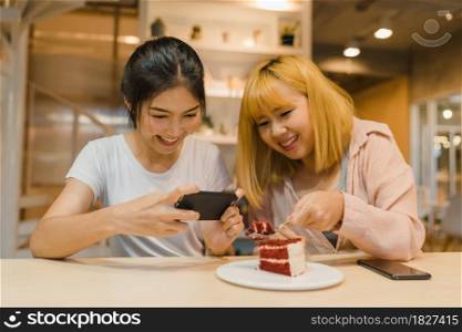 Cheerful young Asia friend using phone taking a photograph food and cake at coffee shop. Two joyful attractive Asian lady together at restaurant or cafe. Holiday activity, or modern lifestyle concept.