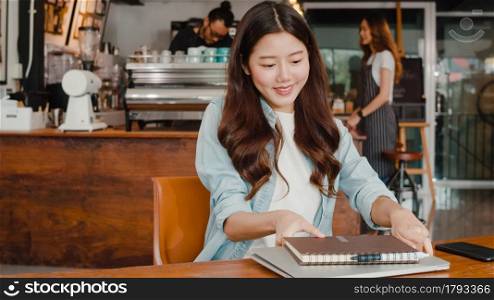 Cheerful Young Asian freelance lady working on laptop at coffee shop. Attractive Japanese businesswoman relax feeling happy in urban cafe or restaurant.