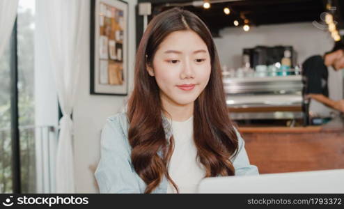 Cheerful Young Asian freelance lady working on laptop at coffee shop. Attractive Japanese businesswoman relax feeling happy in urban cafe or restaurant.