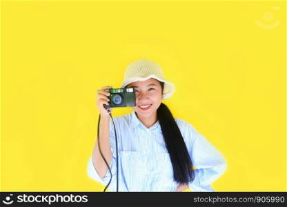 Cheerful young Asian woman portrait fashion smiling and take pictures photographer with vintage film camera on yellow background / Hipster cool girl