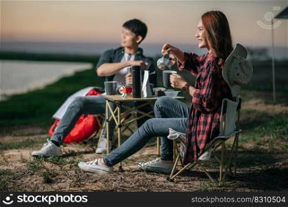 Cheerful Young backpacker couple sitting at front of the tent in forest with coffee set and making fresh coffee grinder while c&ing trip on summer vacation, Selective focus