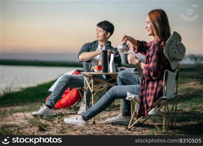 Cheerful Young backpacker couple sitting at front of the tent in forest with coffee set and making fresh coffee grinder while camping trip on summer vacation, Selective focus