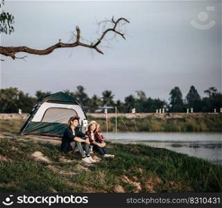 Cheerful Young backpacker couple sitting at front of the tent near lake with coffee set and making fresh coffee grinder while c&ing trip on summer vacation