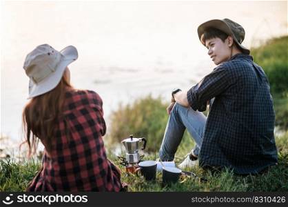 Cheerful Young backpacker couple sitting on grass near lake in early morning and making fresh coffee grinder while c&ing trip on summer vacation