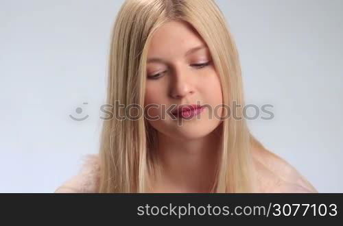 Cheerful young blonde woman slowly lifting up her head, looking mysteriously at the camera and smiling on white background. Positive teenage girl with radiant smile gazing at the cam closeup.