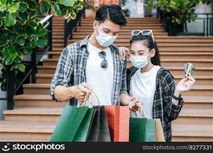 Cheerful Young couple holding multiple paper shopping bag going down stairs of large shopping mall and pretty woman show credit card in hand, They look inside bag with excited