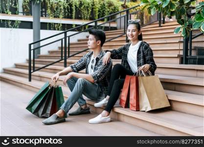 Cheerful Young couple holding multiple paper shopping bag on stairs of large shopping mall,  Lifestyle and shopping concept, copy space