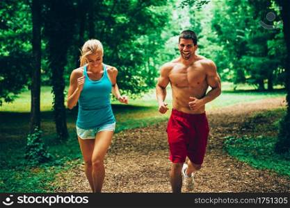 Cheerful young couple jogging in forest