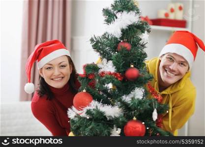 Cheerful young couple looking out from Christmas tree