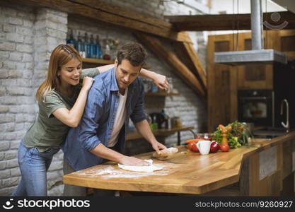 Cheerful young couple making pizza in rustic kitchen together