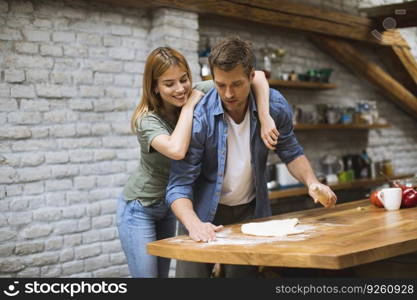 Cheerful young couple making pizza in rustic kitchen together