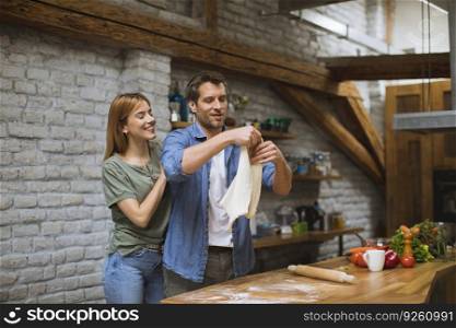 Cheerful young couple making pizza in rustic kitchen together