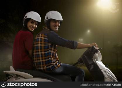 Cheerful young couple riding on a motorbike at night