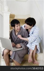 Cheerful young couple sitting on stairway using laptop