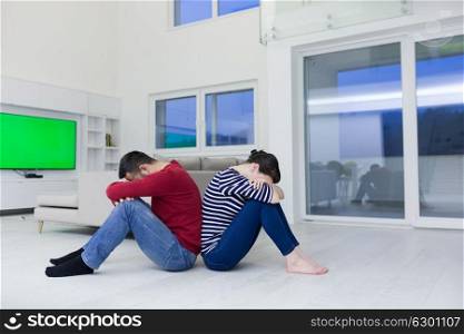 Cheerful young couple sitting with back to each other on floor at home