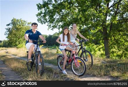 Cheerful young family cycling in meadow at hot sunny day