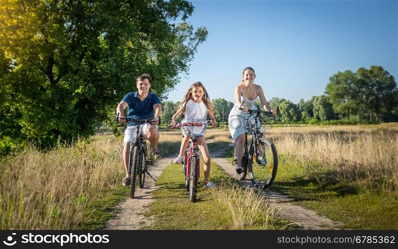 Cheerful young family riding on bicycles at meadow. Concept of family sport