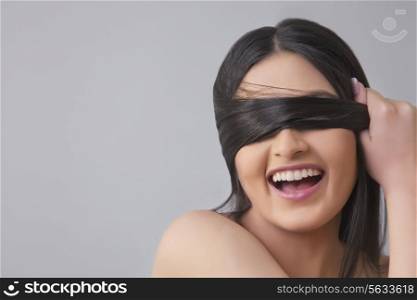 Cheerful young female covering eyes with her hair over colored background