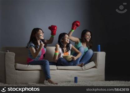 Cheerful young female friends watching boxing match together at home