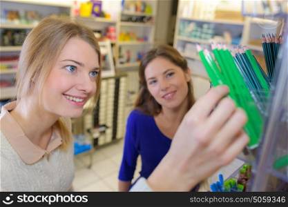 cheerful young girl and friend choosing pencils at a stationary
