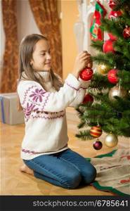 Cheerful young girl decorating Christmas tree at house