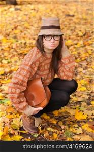 Cheerful young girl with handbag sitting on yellow autumn leaf background