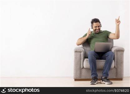 Cheerful young man listening music on headphones and having fun while sitting on sofa
