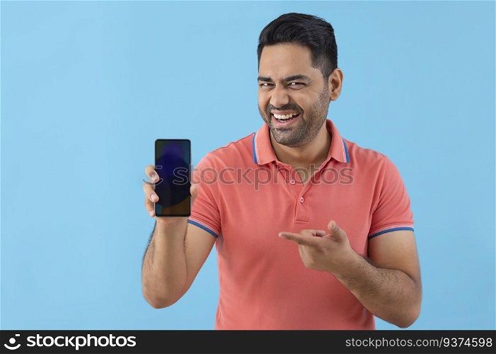 Cheerful young man looking at camera and pointing at Smartphone holding in his hand 