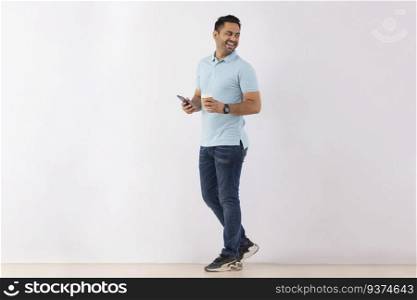Cheerful young man looking back while standing with Smartphone and Coffee against white background