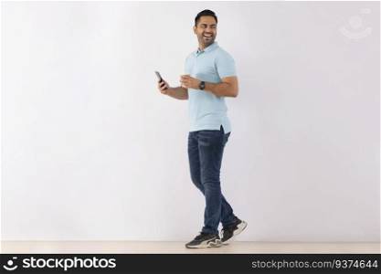 Cheerful young man looking back while standing with Smartphone and Coffee against white background