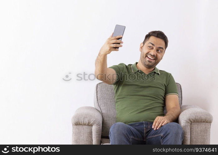Cheerful young man taking selfie by using Smartphone while sitting on sofa