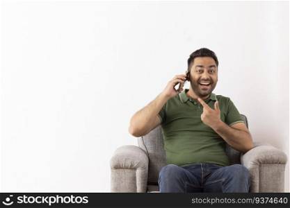 Cheerful young man talking on Smartphone while sitting on sofa