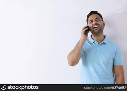 Cheerful young man talking on Smartphone while standing against white background