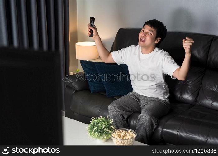 cheerful young man watching sport TV with arm raised on sofa at night