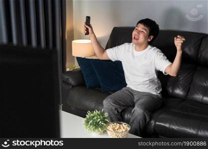 cheerful young man watching sport TV with arm raised on sofa at night