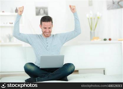 cheerful young man with laptop raising hands indoors