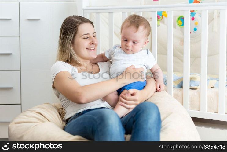 Cheerful young mother reading book to her baby boy at living room