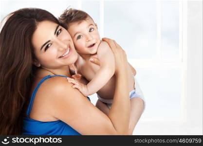 Cheerful young mother with her cute little son playing at home, with pleasure spending time together, happy family life