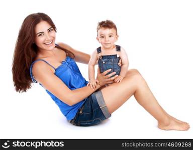 Cheerful young mother with her cute little son sitting on the floor and playing in the studio, isolated on white background, happy family together