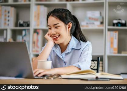 Cheerful young pretty woman sitting and use laptop computer and textbook to work or learning online, holding coffee mug in hand and smile with happy