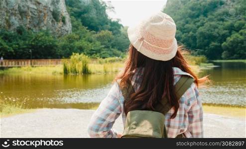 Cheerful young traveler Asian lady with backpack walking at the mountain lake. Korean teen girl enjoy her holidays adventure feeling happy freedom. Lifestyle travel and relax in free time concept.