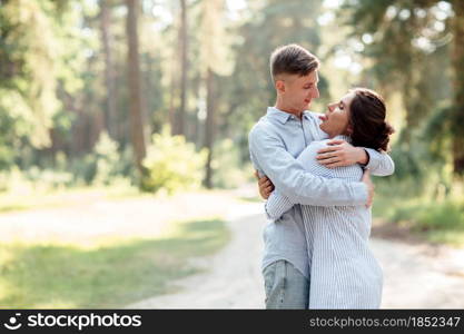 Cheerful young woman and man are hugging outdoors in summer park. Dating and romantic vacation. couple in love gently looking at each other on sunny day. Love and relationships between young people.. Cheerful young woman and man are hugging outdoors in summer park. Dating and romantic vacation. couple in love gently looking at each other on sunny day. Love and relationships between young people