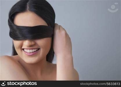 Cheerful young woman covering eyes with her hair over colored background